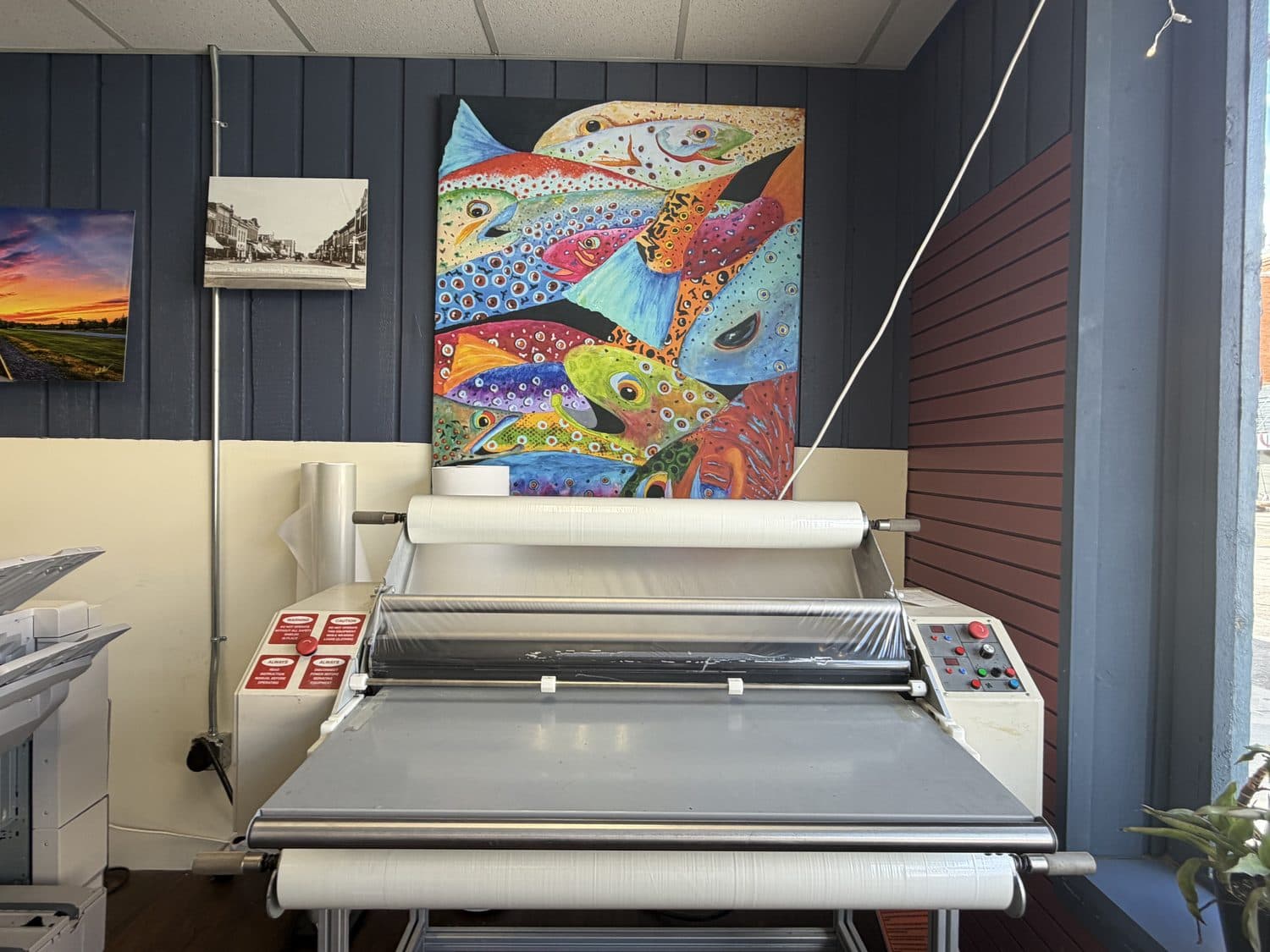 A painted canvas of Wyoming trout on the shop wall above the wide-format laminator