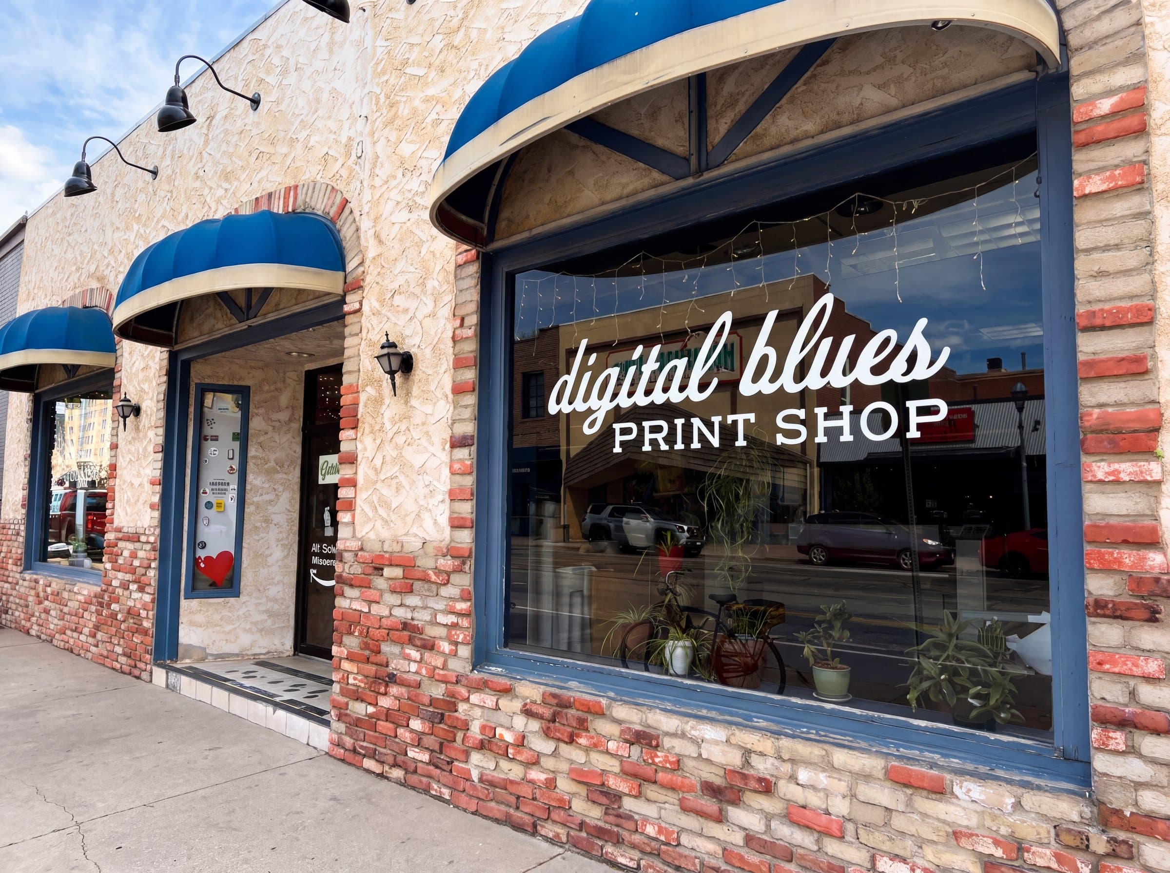 The digital blues Print Shop storefront on Grand Avenue: blue awnings over an arched window with the shop name lettered across the glass